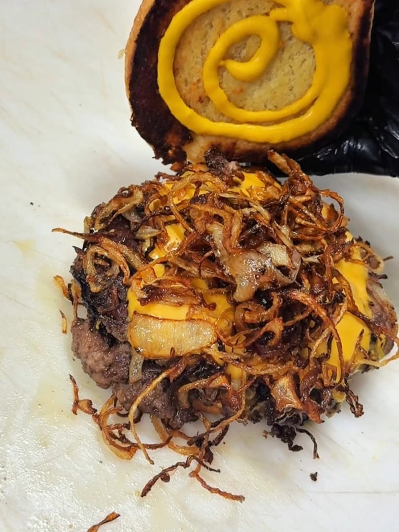 A burger patty with melted cheese and crispy fried onions, with a mustard-swirled bun above.