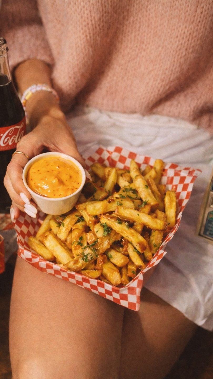 A person holds a small cup of orange dipping sauce next to a basket of seasoned french fries.
